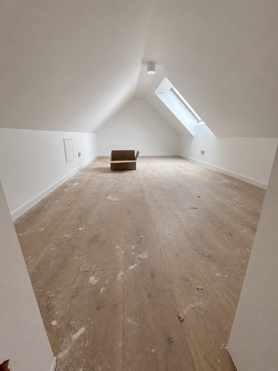 Im renovierten Dachboden liegen noch Staub, helle Renovierungsrückstände und kleine Verschmutzungen auf dem Boden. Ein Karton steht im hinteren Raumbereich