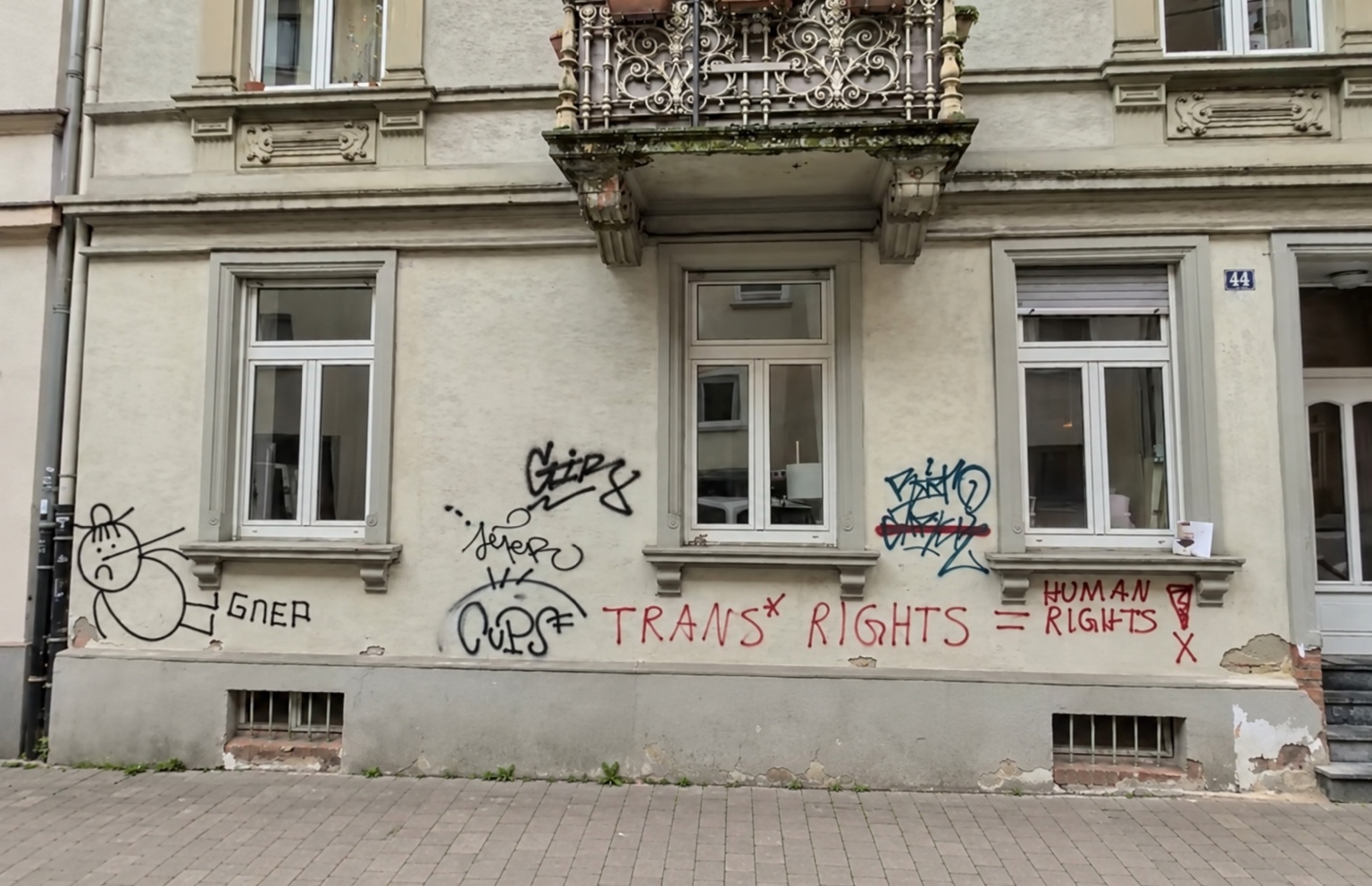 Vorher: helle Hausfassade mit schwarzen, roten und blauen Graffiti unter den Fenstern