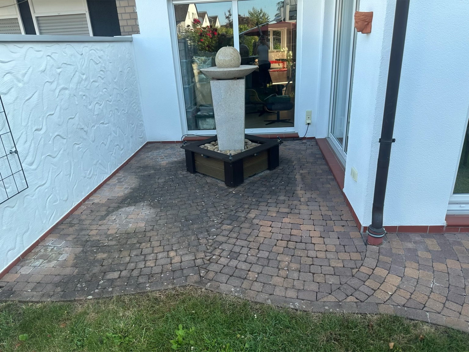 Gepflasterte Terrasse rund um einen Zierbrunnen vor der professionellen Reinigung mit deutlich sichtbaren Verschmutzungen und Ablagerungen